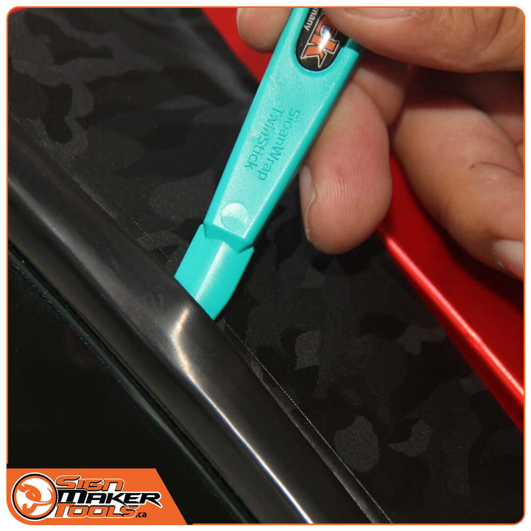 Hand using WrapStick tool to apply vinyl wrap along automotive trim